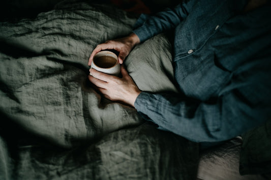 a person holding a cup of coffee on top of a bed