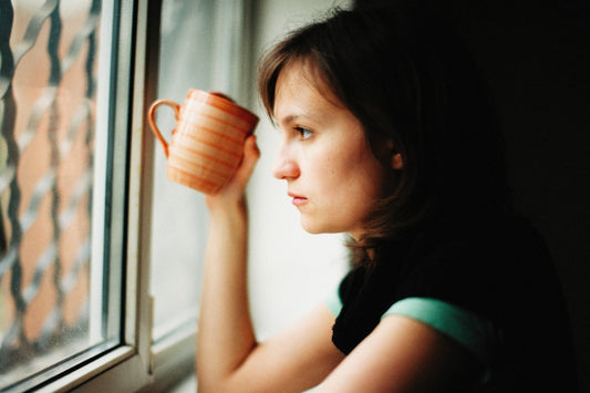 a woman holding a cup looking out a window