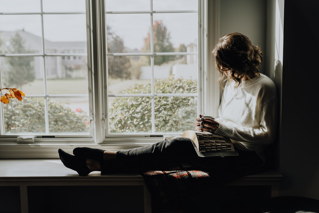 A woman sitting on a window sill reading a book